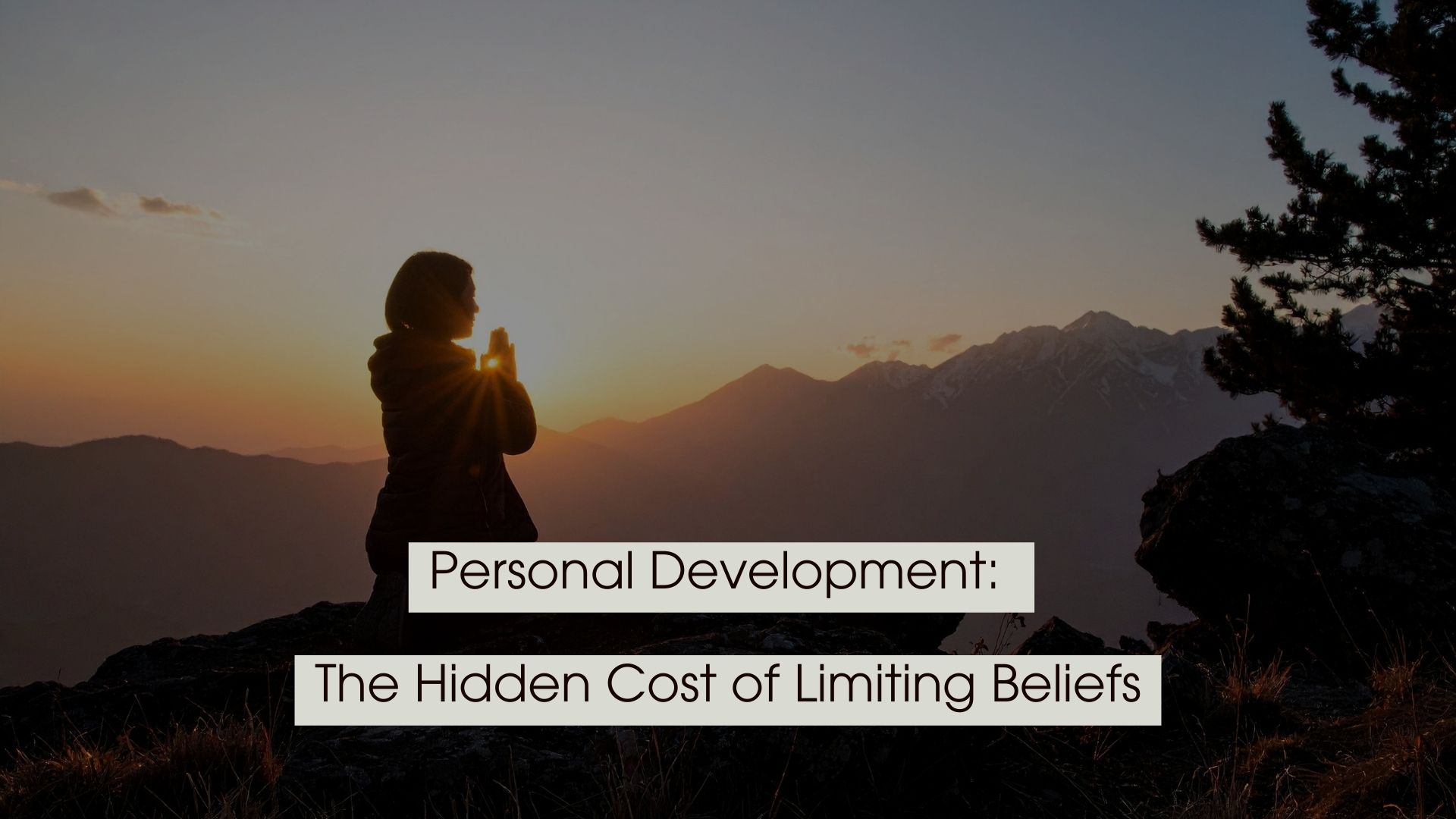 Silhouette of a person standing on a mountain at sunrise with hands clasped in reflection, with the text “Personal Development: The Hidden Cost of Limiting Beliefs” displayed across the image.