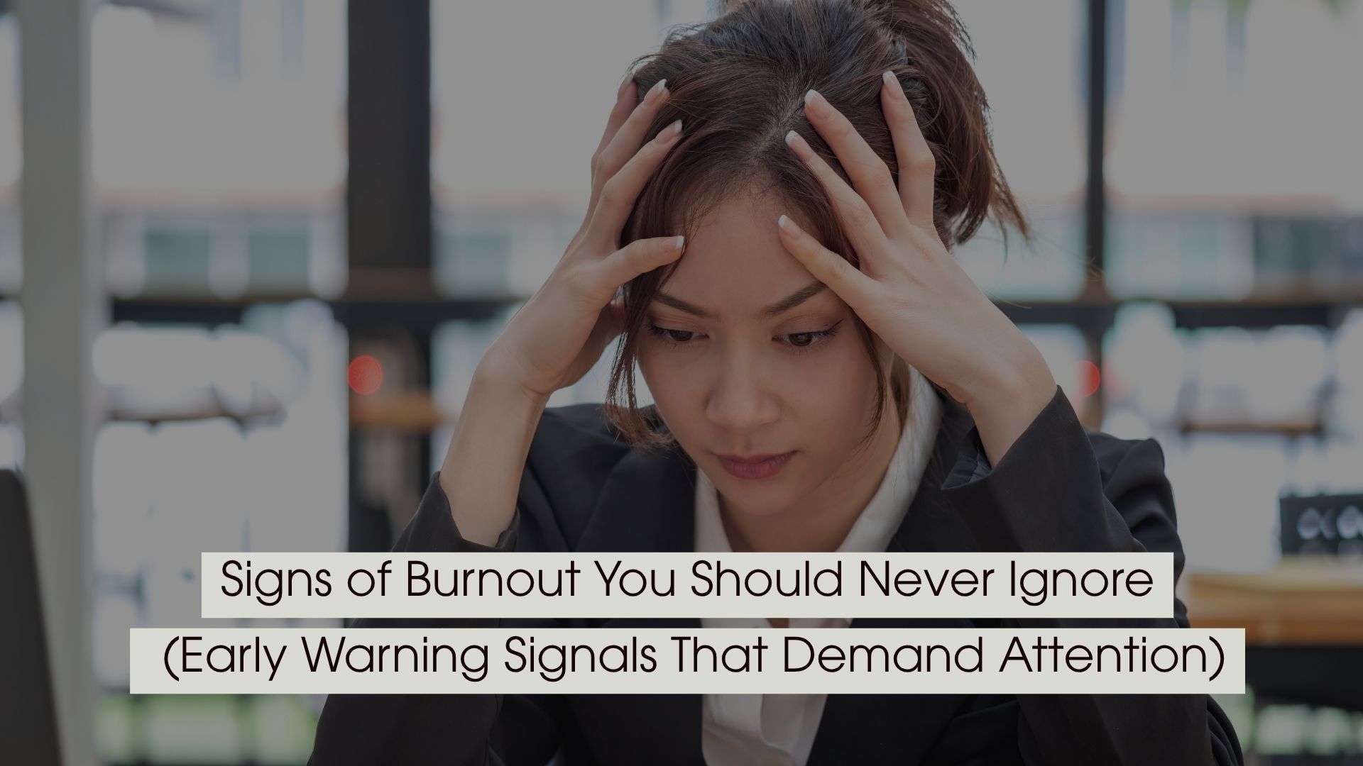Person sitting at a desk holding their head with both hands, appearing stressed and overwhelmed, symbolizing burnout and mental fatigue, with the text “Signs of Burnout You Should Never Ignore (Early Warning Signals That Demand Attention)” displayed across the image.
