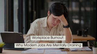 Office worker sitting at a desk looking stressed while holding his forehead and reviewing documents, with the text “Workplace Burnout: Why Modern Jobs Are Mentally Draining” displayed across the image.