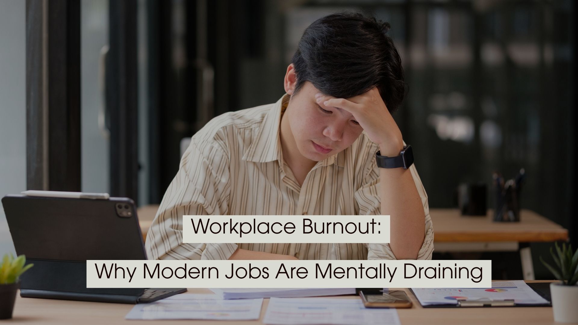 Office worker sitting at a desk looking stressed while holding his forehead and reviewing documents, with the text “Workplace Burnout: Why Modern Jobs Are Mentally Draining” displayed across the image.