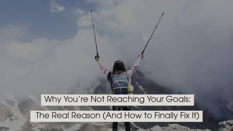 Hiker standing on a mountain summit with arms raised in victory, symbolizing achievement and overcoming challenges, with the text “Why You’re Not Reaching Your Goals: The Real Reason (And How to Finally Fix It)” displayed across the image.