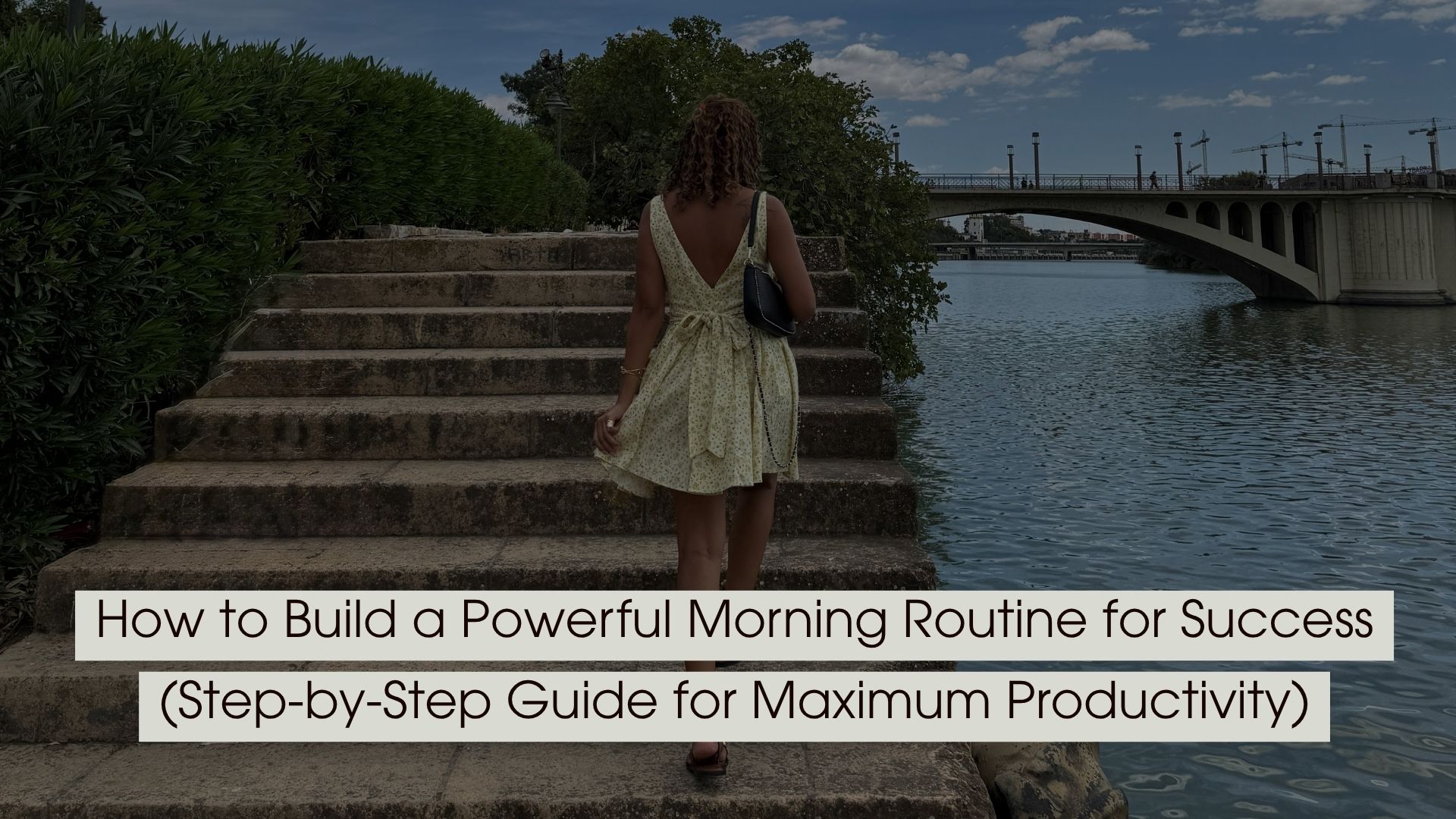 Woman walking up stone steps beside a river toward a bridge, symbolizing progress and fresh starts, with the text “How to Build a Powerful Morning Routine for Success (Step-by-Step Guide for Maximum Productivity)” displayed across the image.