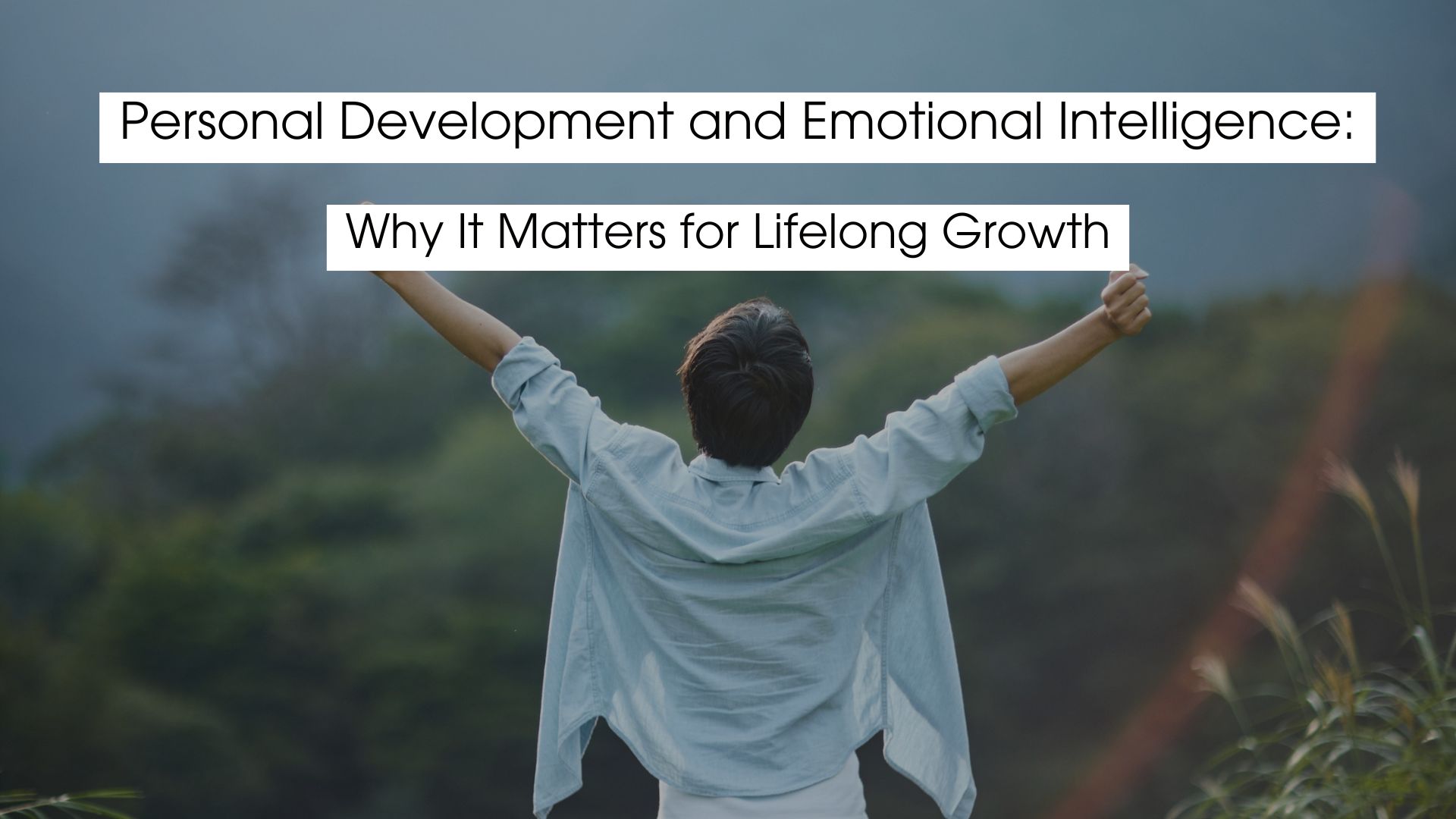 A person standing outdoors with arms raised, facing a scenic view of green hills and misty mountains, symbolizing personal growth and emotional empowerment.