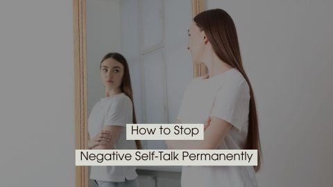 Young woman standing with arms crossed while looking at her reflection in a mirror, with the text “How to Stop Negative Self-Talk Permanently” displayed across the image.