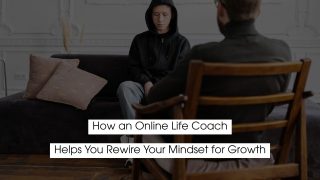 A person in a black hoodie sits on a couch with head slightly lowered, facing a life coach seated across from them in a chair, suggesting a counseling or coaching session. Overlaid text reads: ‘How an Online Life Coach Helps You Rewrite Your Mindset for Growth.’