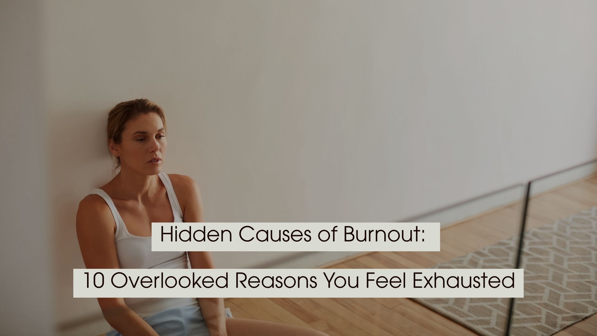 Tired-looking woman sitting on the floor against a wall in a quiet room, with the text “Hidden Causes of Burnout: 10 Overlooked Reasons You Feel Exhausted” displayed across the image.