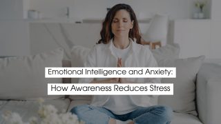 Woman sitting cross-legged on a sofa with eyes closed and hands in a prayer position, practicing mindfulness and calm breathing, symbolizing emotional intelligence, anxiety relief, stress reduction, and emotional awareness.