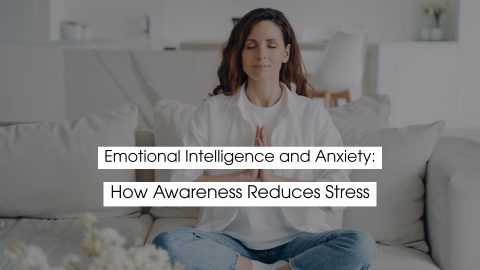 Woman sitting cross-legged on a sofa with eyes closed and hands in a prayer position, practicing mindfulness and calm breathing, symbolizing emotional intelligence, anxiety relief, stress reduction, and emotional awareness.