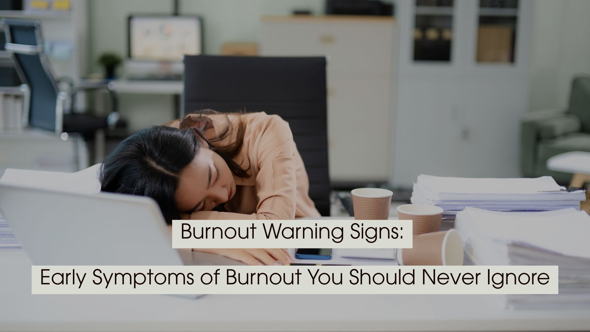 Exhausted office worker resting her head on a desk surrounded by paperwork and coffee cups, with the text “Burnout Warning Signs: Early Symptoms of Burnout You Should Never Ignore” displayed across the image.