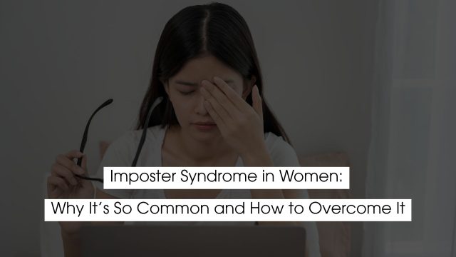 Woman sitting at a desk with eyes closed and hand on her forehead, holding glasses, appearing stressed or overwhelmed, representing imposter syndrome and self-doubt in women.