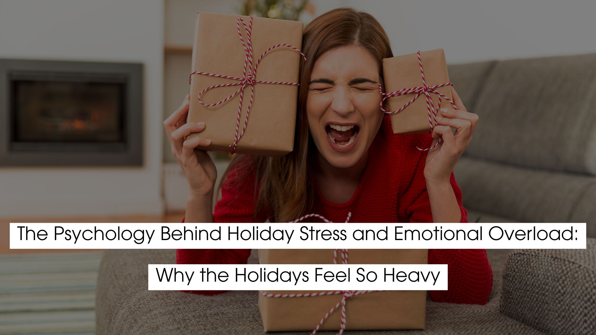 A woman sitting on the floor, holding two gift boxes with red ribbons, looking overwhelmed and stressed. She is wearing a red sweater, with a frustrated expression on her face, possibly due to holiday-related pressure. The image has a cozy indoor setting with a fireplace in the background. The text on the image reads: "The Psychology Behind Holiday Stress and Emotional Overload: Why the Holidays Feel So Heavy."